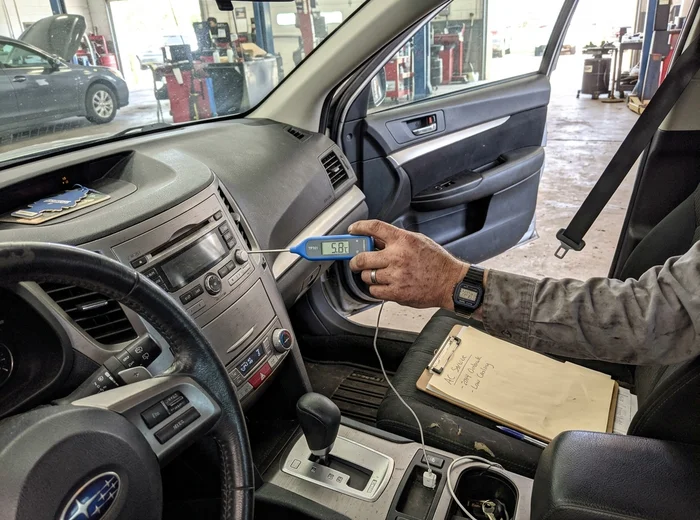 Thermometer in a dashboard vent confirming outlet temperature after AC repair