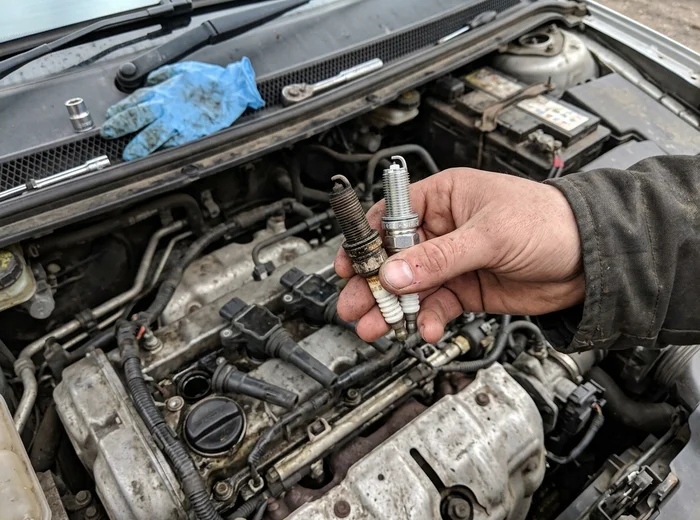 Carbon-fouled spark plug next to a clean replacement plug