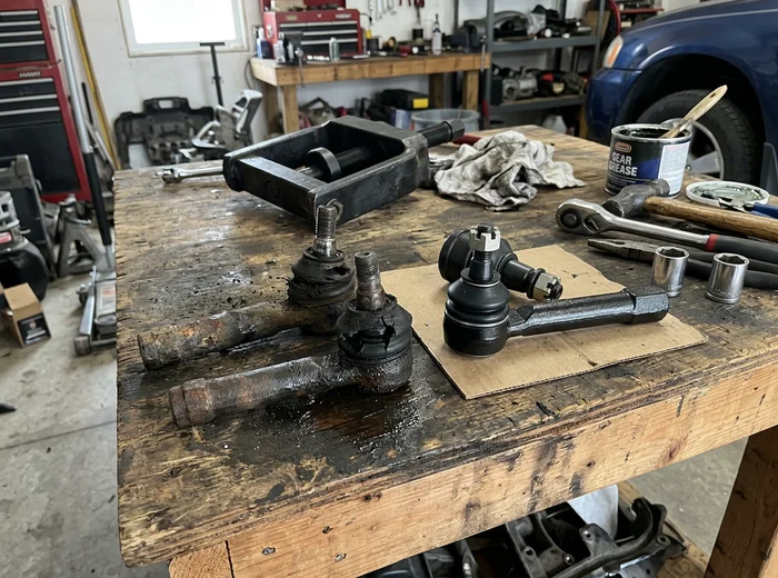 Worn tie rod end and ball joint beside their replacements